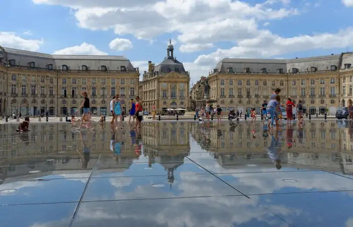 Bir grup insan Fransa, Bordeaux'daki Miroir d'eau'nun parlak su yüzeyinin keyfini çıkarıyor.